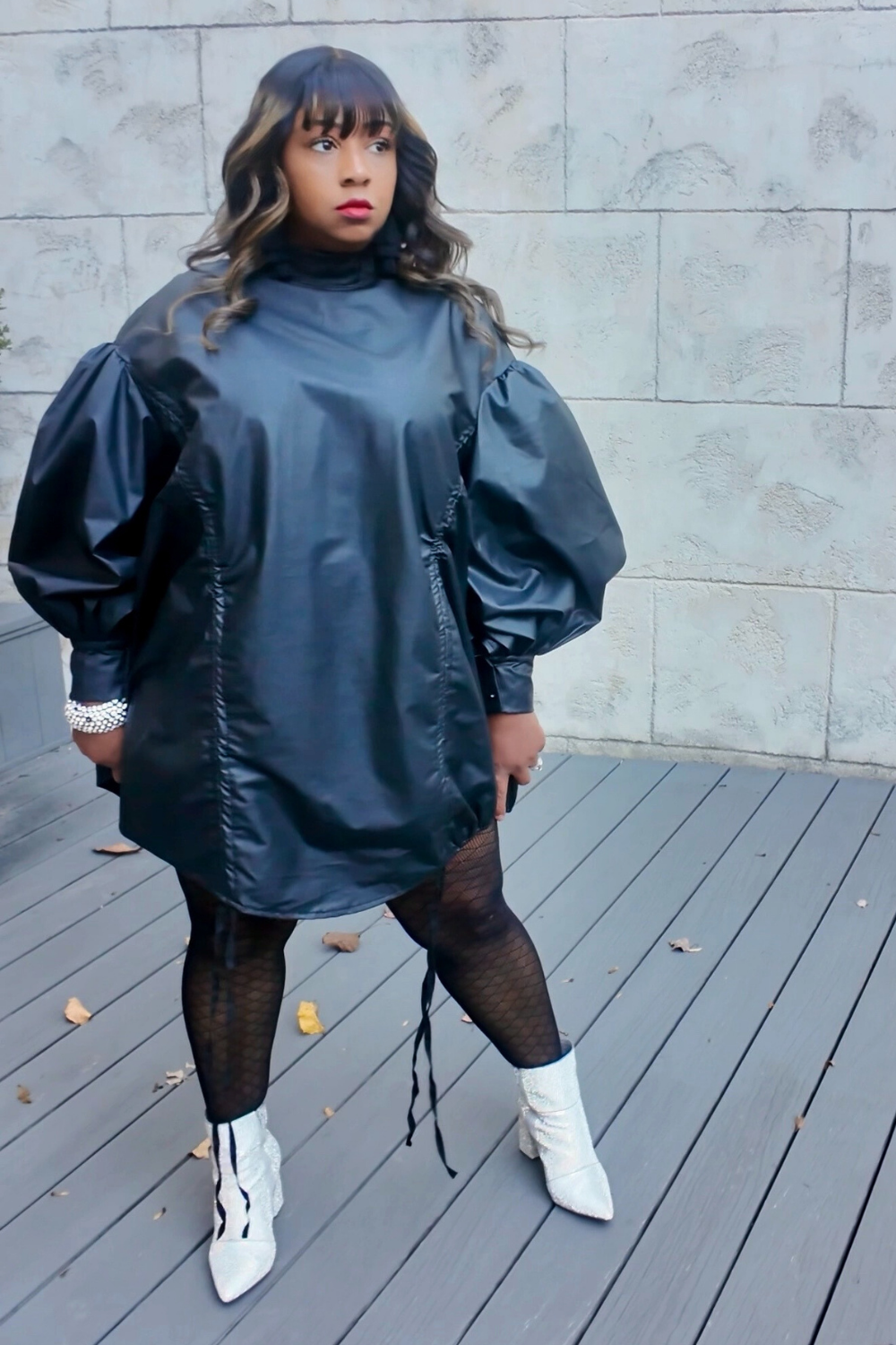 Model wearing The Luxe Parachute Dress — a black high-neck mini dress with voluminous puff sleeves, cinched waist belt, and gold pointed heels by Sassie Girl Fashion.