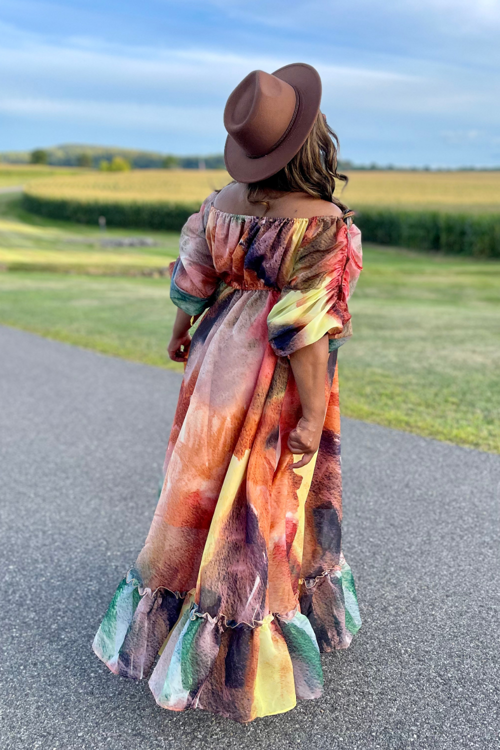 Person wearing a colorful dress and hat standing on a road with a scenic background