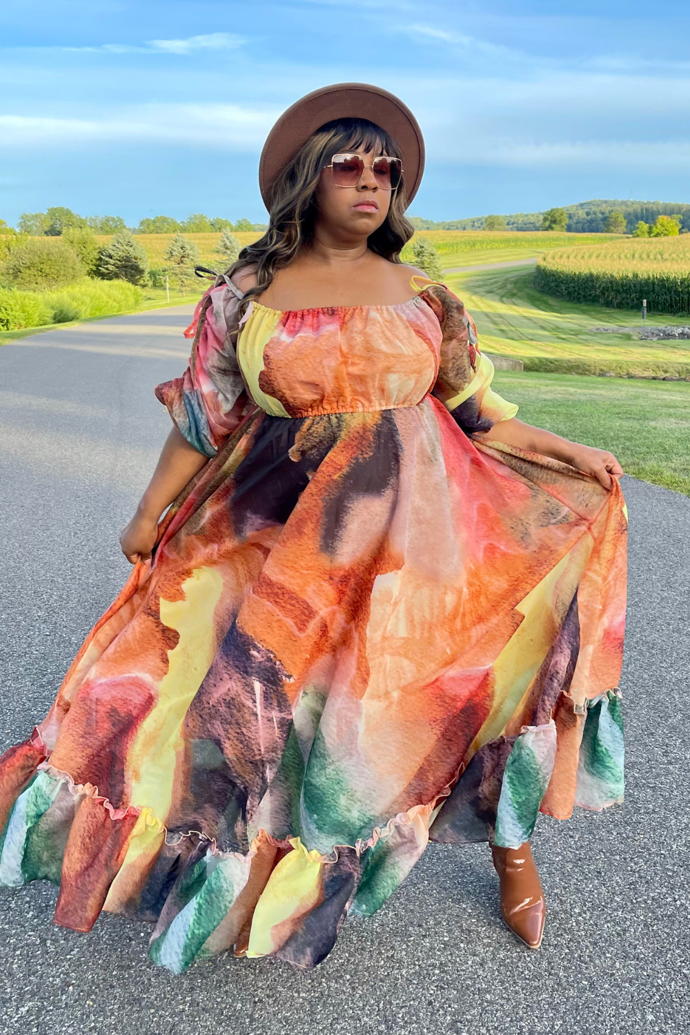 Woman in a colorful dress and hat standing on a road with a scenic background