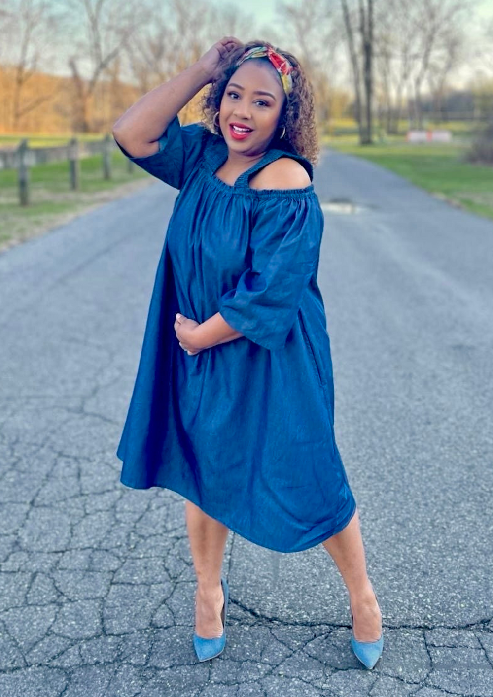 Woman wearing an off-shoulder denim flare dress with statement sleeves and a red belt, styled outdoors for a spring fashion look.