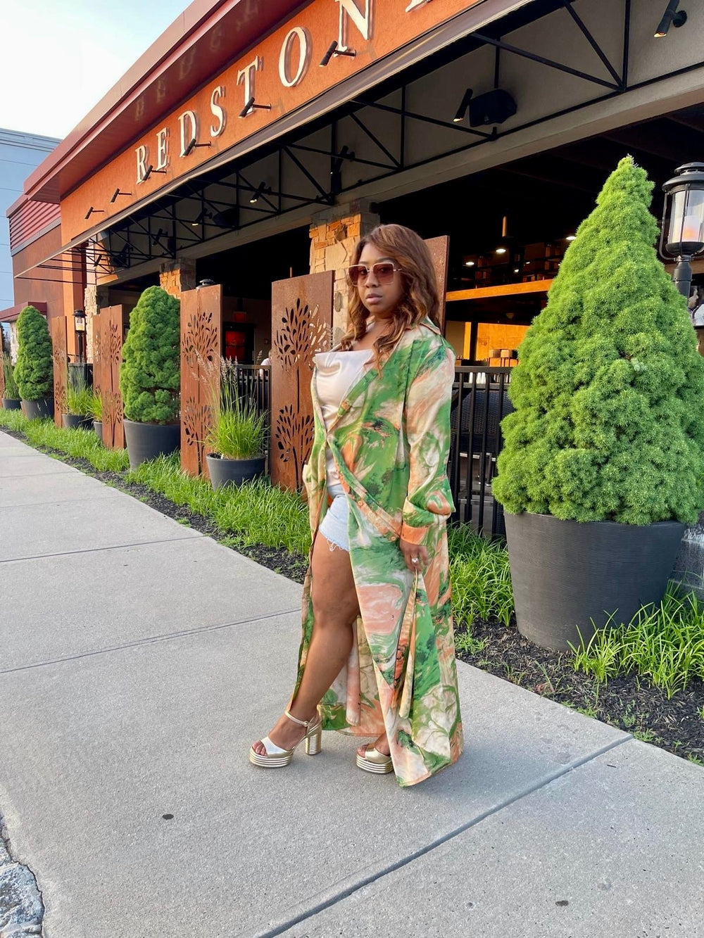 Woman wearing a flowy green and orange floral print Emerald Bloom Dress with high slit, posing confidently outside a restaurant.