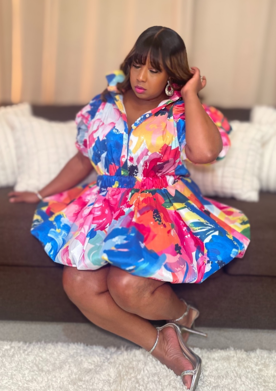 Woman wearing a colorful dress sitting on a couch.