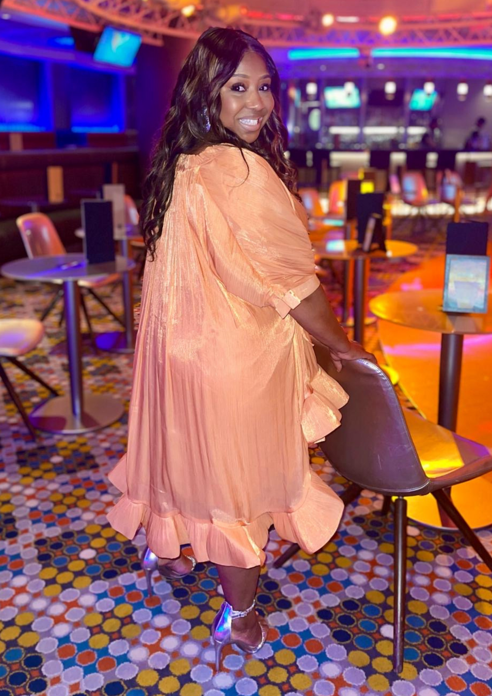 Woman wearing a flowing peach-orange ruffle dress with a cinched waist and high-low hemline
