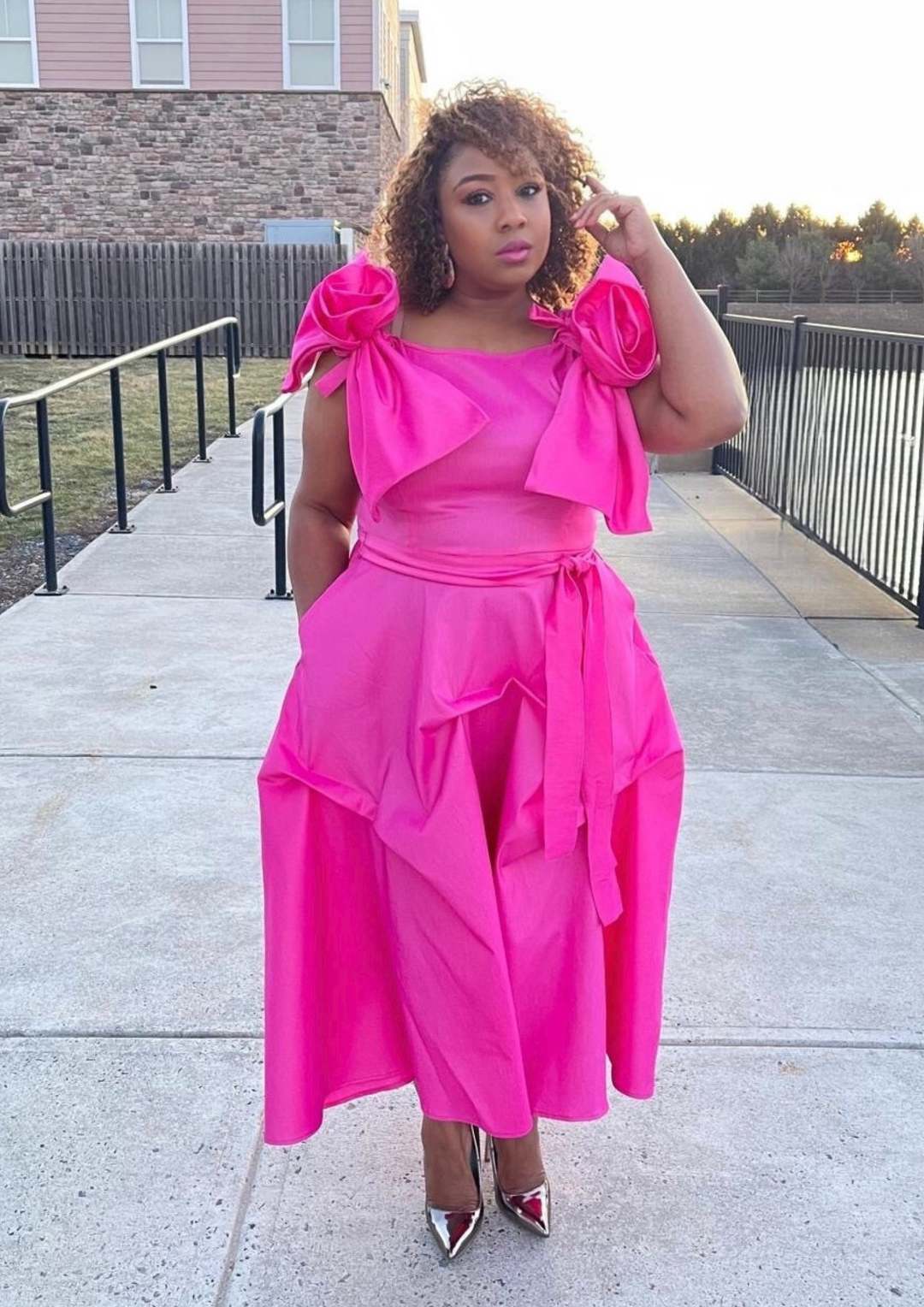 Woman wearing a vibrant fuchsia midi dress with detachable oversized shoulder bows and a removable waist belt, styled both with and without the accessories to show its versatile design.