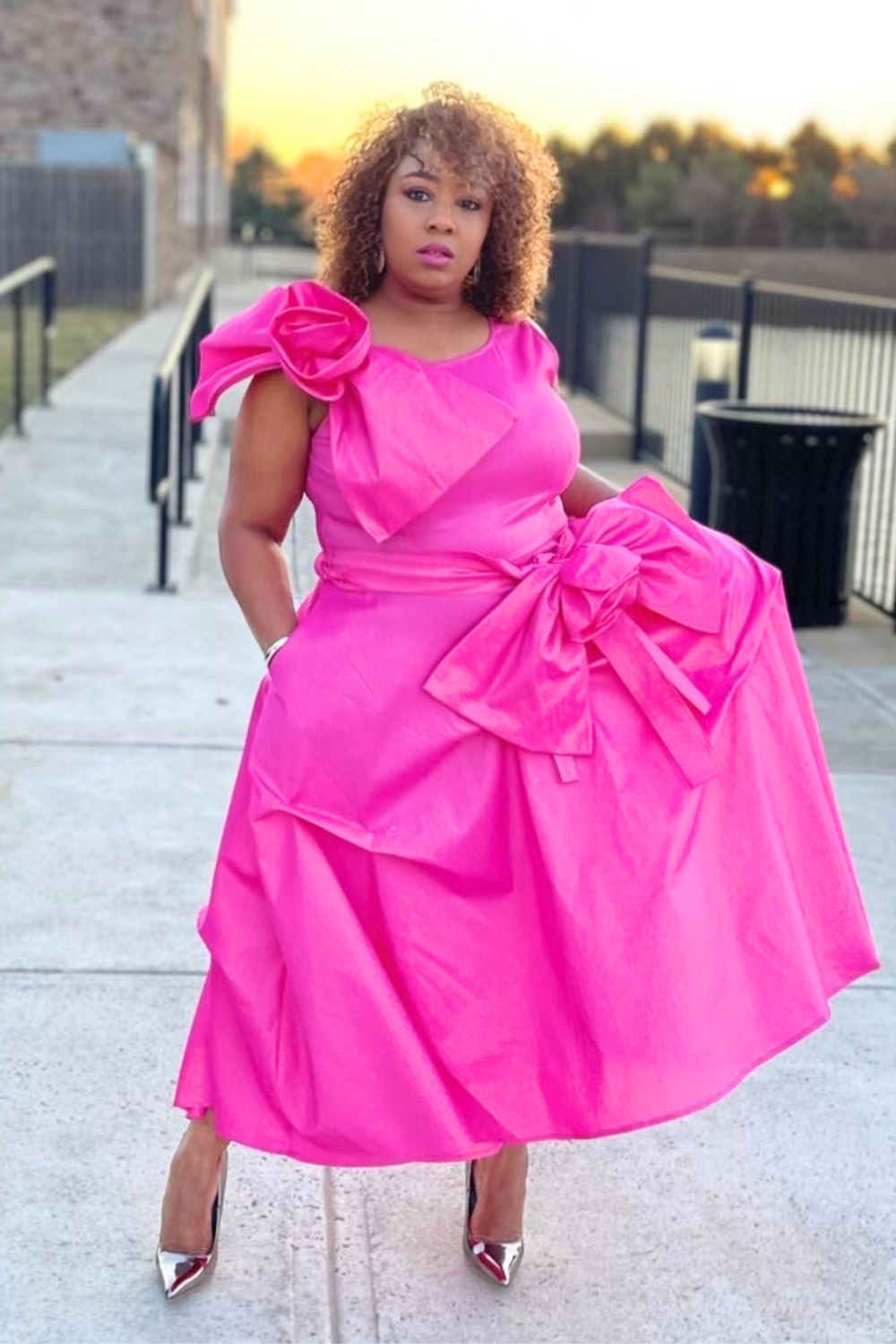 Woman wearing a bright pink dress with large bows outdoors.