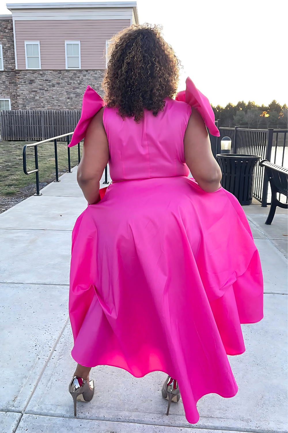 A woman wearing a bright pink dress with ruffled sleeves is standing on a deck.