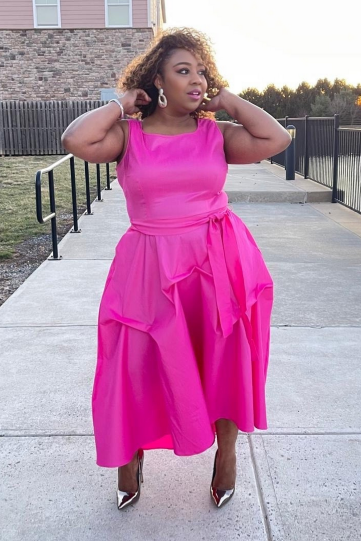 A woman wearing a bright pink dress with ruffled sleeves is standing on a deck.