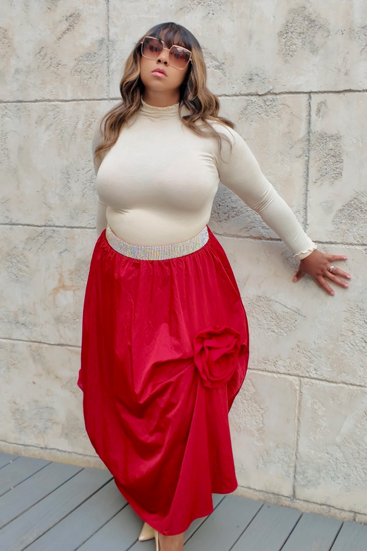 Woman wearing a beige top and red skirt against a stone wall.
