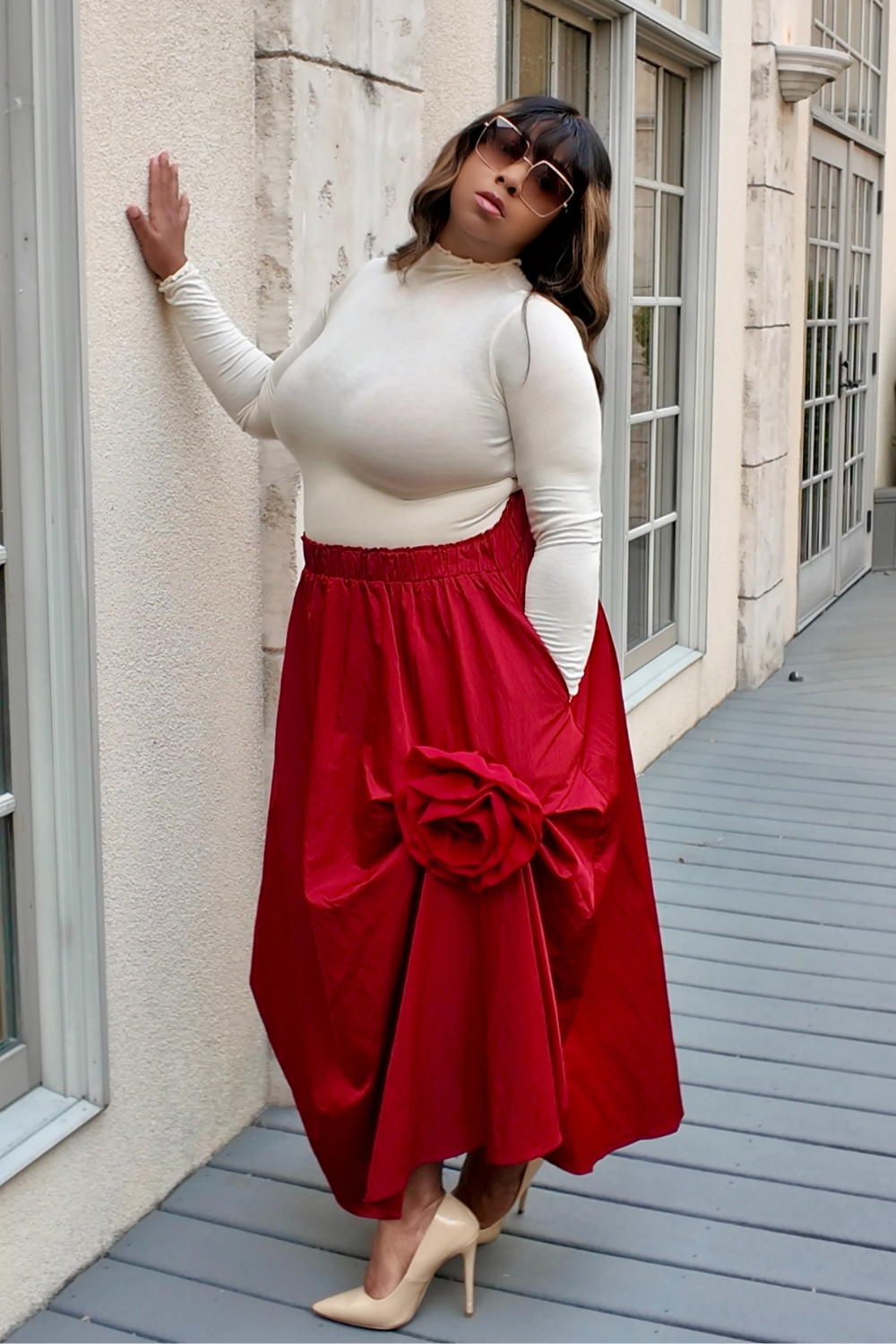 Woman wearing a white top and red skirt standing against a building.