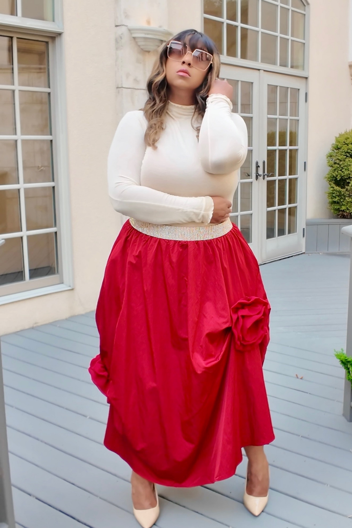 Woman wearing a white top and red skirt standing in front of a building.