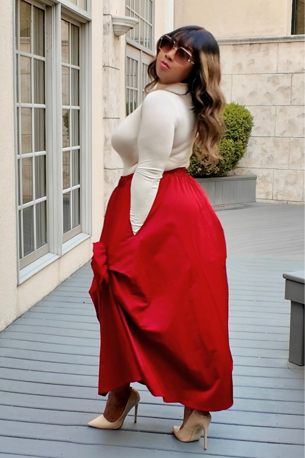 Woman wearing a white top and red skirt standing on a wooden deck.