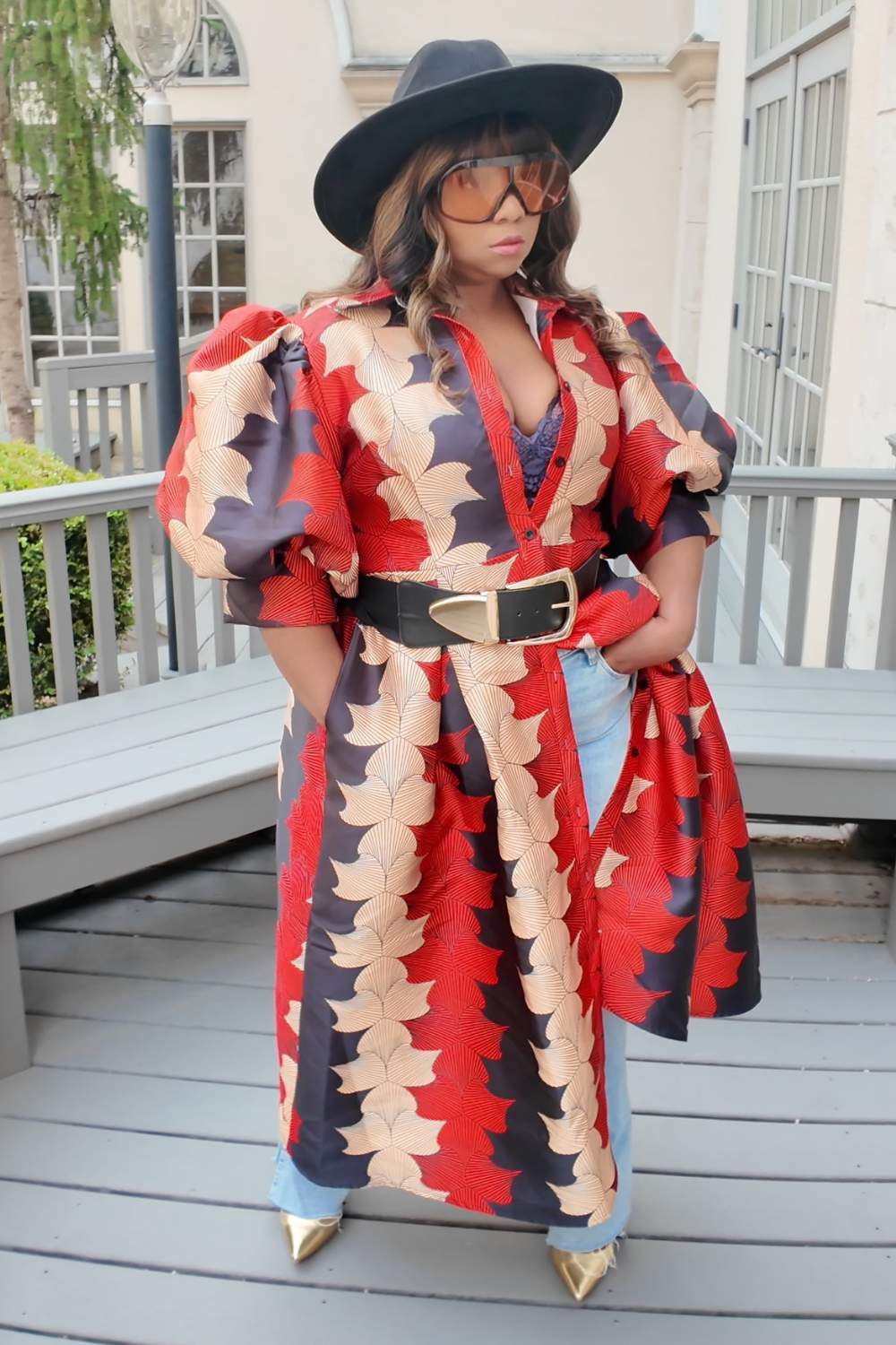 A woman wearing a colorful outfit with a red and black patterned dress and hat, standing on a Terrace.