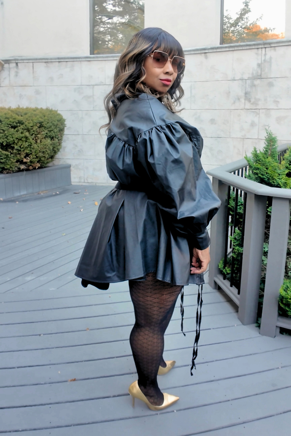 Model wearing The Luxe Parachute Dress — a black high-neck mini dress with voluminous puff sleeves, cinched waist belt, and gold pointed heels by Sassie Girl Fashion.