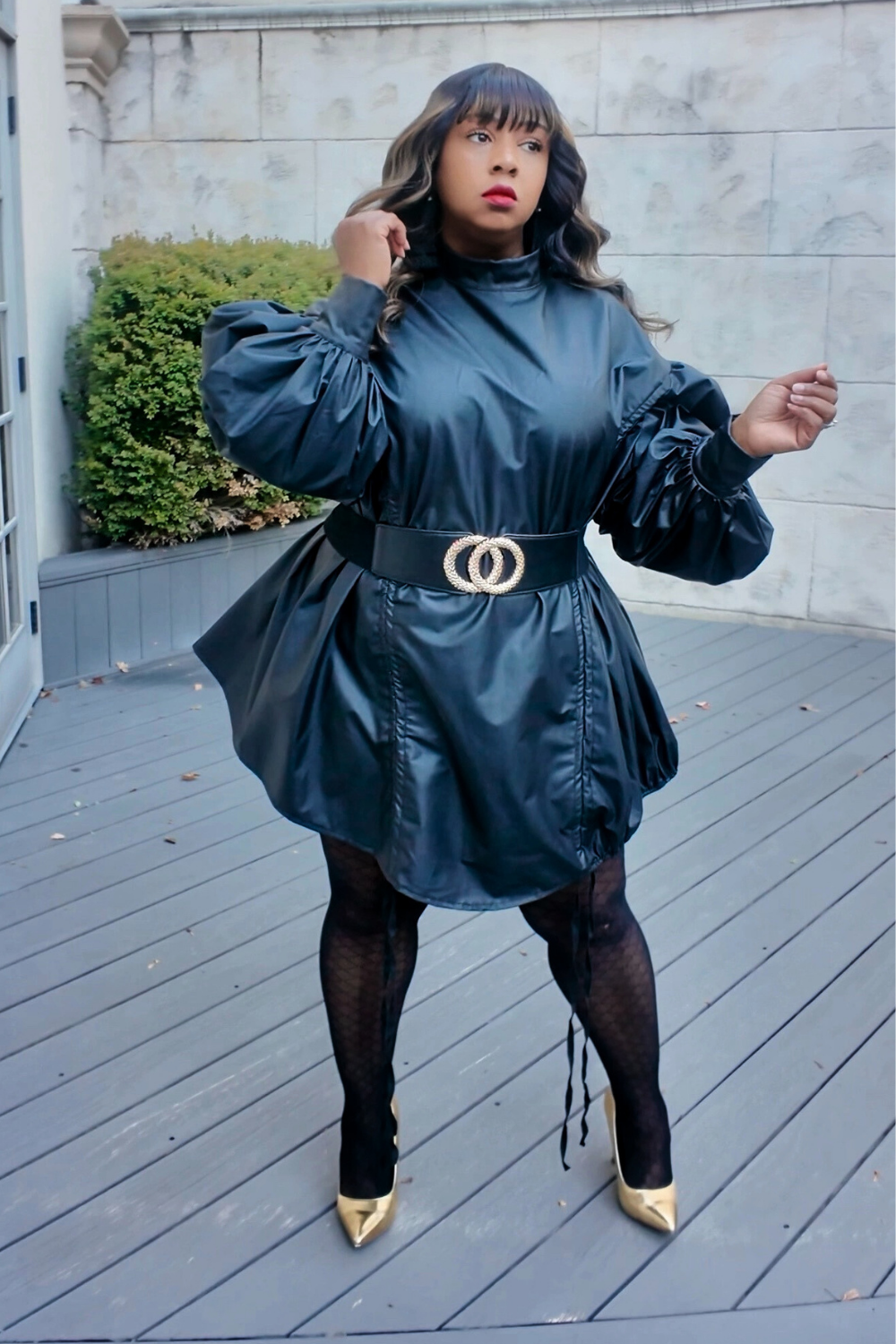 Model wearing The Luxe Parachute Dress — a black high-neck mini dress with voluminous puff sleeves, cinched waist belt, and gold pointed heels by Sassie Girl Fashion.