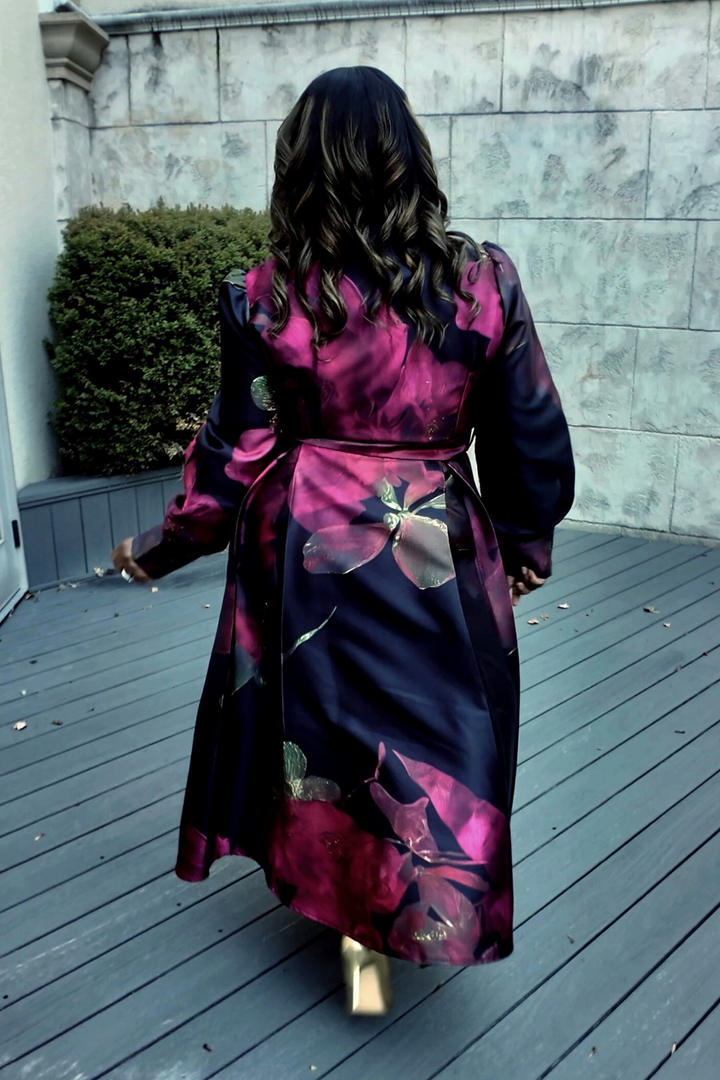 A woman wearing a colorful floral dress standing on a wooden deck with a stone wall background